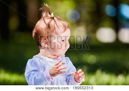 Close-up summer portrait of beautiful baby girl on the lawn in the park. Cute little girl in the white dress. Summer or spring season in the city park. Warm sunshiny day. Concept of the happy children.