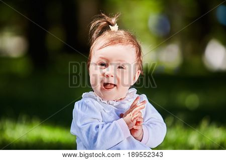 Close-up summer portrait of beautiful baby girl on the lawn in the park. Cute little girl in the white dress. Summer or spring season in the city park. Warm sunshiny day. Concept of the happy children.