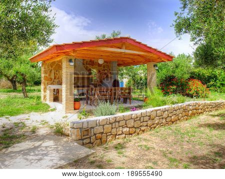 VASILIKOS, ZAKYNTHOS ISLAND, GREECE, MAY 30, 2016: Beautiful view on summer pavilion with fireplace for BBQ barbecue next to Greek Porto Gerakas villas for guests in amazing olive trees garden