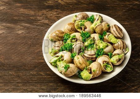 A photo of escargots a la bourguignonne, a plate of snails with the typical French green sauce of garlic and herb butter, on a rustic texture with a place for text