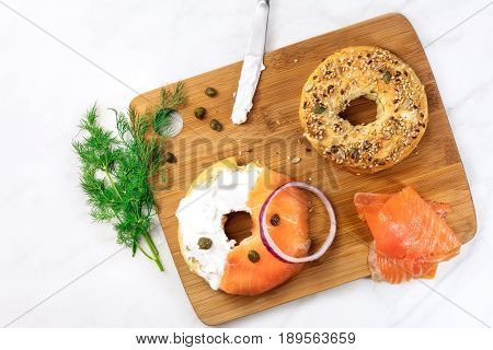 Bagel ingredients. Lox, purple onions, capers, dill, and the buns, shot from above on a wooden board and a white marble background in the process of making, with a place for text