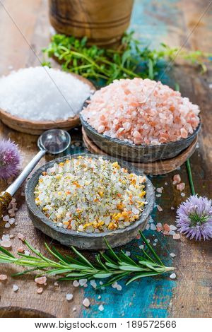 Different types of natural salt in stone bowls on wooden surface. White sea salt pink Himalayan salt Spiced salt with rosemary