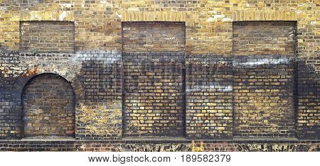 Aged brick wall with four arched bricked up windows with space for text.