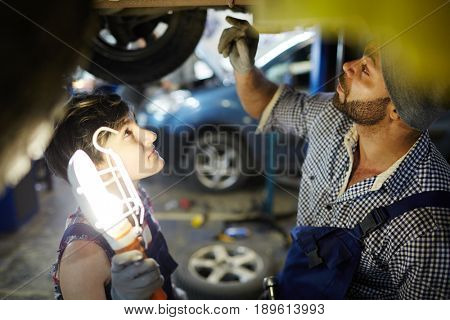 Repairman in uniform showing his trainee how to change tire