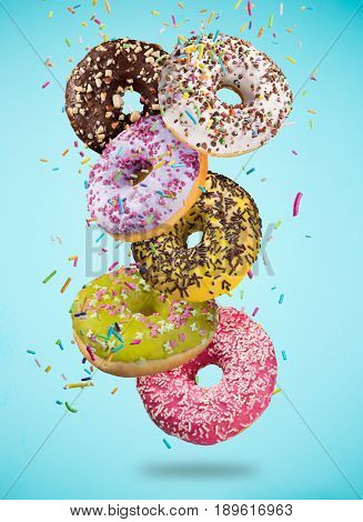 Tasty doughnuts in motion falling on pastel blue background, close-up.