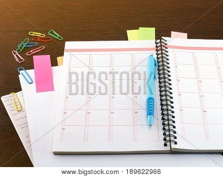 notebook, blue pen, sticky notes, blank paper, financial documents and colorful paperclip on dark brown wooden table floor, close-up diary calendar for financial planning