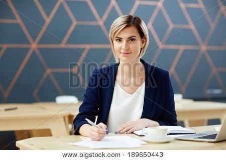 Young newsreader sitting by workplace in studio