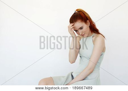 Studio portrait of attractive young Caucasian redhead female looking away with cute and shy smile. Headshot of attractive charming young female student looking