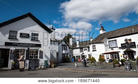 HAWKSHEAD UK - 23 APRIL 2017: The crowded whitewashed architecture of the village of Hawkshead in the heart of the English Lake District with tourists outside a small business shop and hotel.