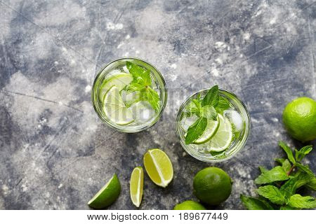 Mojito Cuba cocktail non alcohol drink two highballs, summer tropical vacation beverage with rum, peppermint mint, lime juice, soda water, sugar and crushed ice on concrete background. Top view