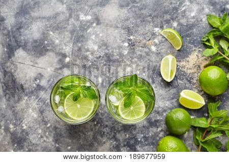 Mojito cocktail traditional alcohol bar drink top view copy space two highball glass, summer tropical vacation beverage with rum, citrus slice, mint, lime juice, soda water and ice on concrete table.