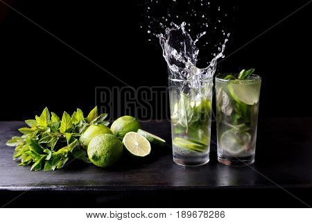 Mojito traditional beach refreshing cocktail alcohol drink in glass with splash, bar preparation soda water, lime, mint leaves, sugar, and rum. Dark black background with copy space for text