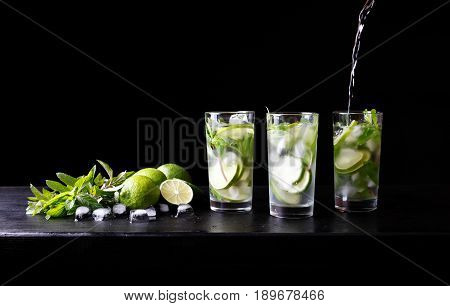 Mojito preparation summer vacation refreshing tropical cocktail non alcohol drink in glass with soda water, lime juice, mint leaves, sugar, ice and rum. Dark black background with copy space text