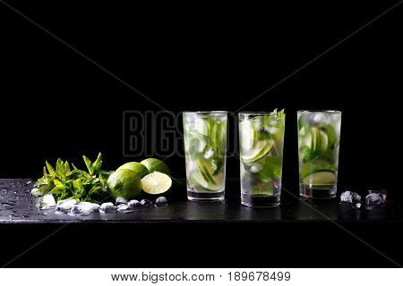Mojito summer party refreshing tropical cocktail non alcohol drink in glass with soda water, lime juice, mint leaves, sugar, ice and rum. Dark black background with copy space text