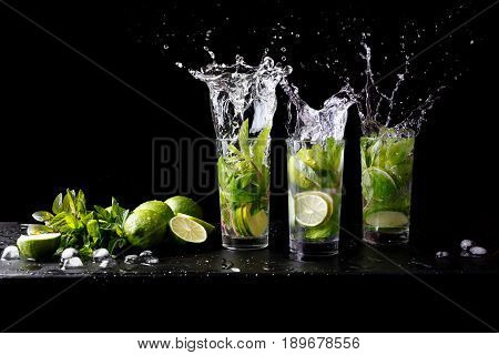 Mojito summer beach refreshing tropical cocktail splash in glass highball alcohol drink with soda water, lime juice, mint leaves, sugar, ice and rum. Dark black background with copy space text