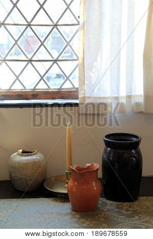 Vertical image of large pottery jugs and tapered candle set at base of curtained window
