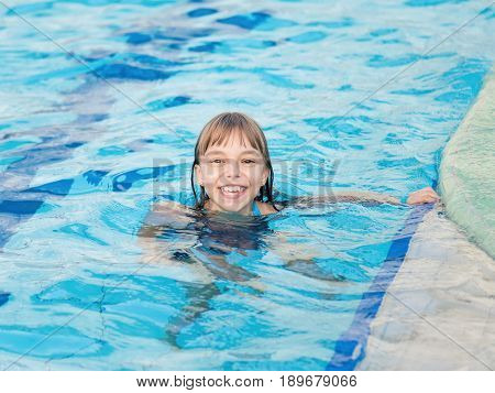 Close-up portrait of happy girl in the swimming pool at aquapark. Cute child having fun enjoyable time on vacation. Looking at camera.