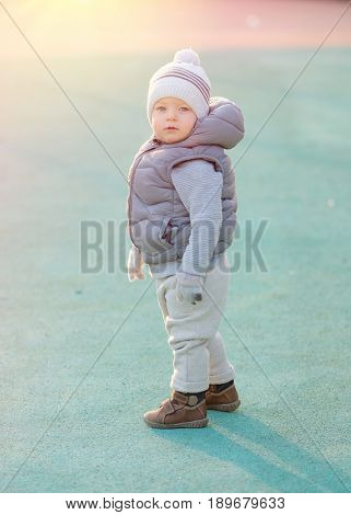 Portrait of toddler child in warm vest jacket outdoors. One year old baby boy wearing vest jacket at playground during sunset. 