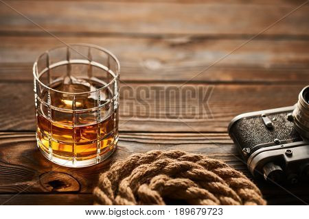 Glass of whiskey and vintage old 35mm rangefinder camera on wooden background
