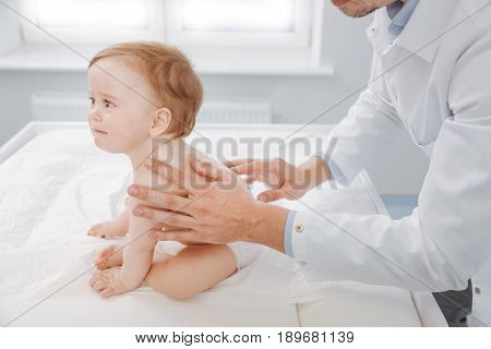 Not nice at all. Joyless concerned emotional child sitting on special table and crying while doctor trying helping him and massaging his back