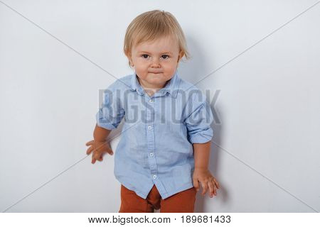 portrait of smiling cute little blonde boy near white wall