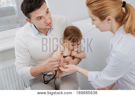 Let me taste it. Wonderful friendly positive pediatrician talking to patients father while the child having fun with her stethoscope