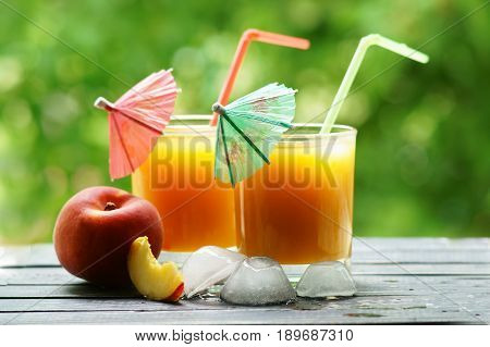 Two glasses of peach juice with a red and green umbrella and tubes on a wooden board with ice.