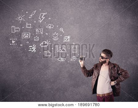An elegant hipster guy trying to use a vintage camera with camera settings icons drawn on wall, like flash, white balace or ISO value concept