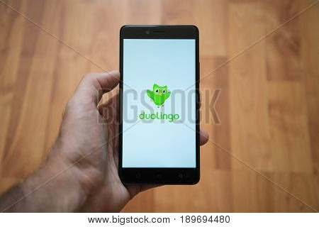 London, United Kingdom, june 5, 2017: Man holding smartphone with Duolingo logo on the screen. Laminate wood background.
