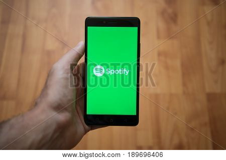 London, United Kingdom, june 5, 2017: Man holding smartphone with Spotify LOGO on the screen. Laminate wood background.