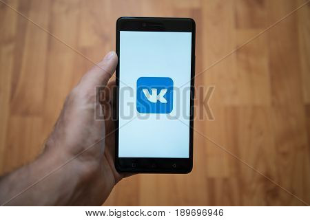 London, United Kingdom, june 5, 2017: Man holding smartphone with Vkontakte LOGO on the screen. Laminate wood background.
