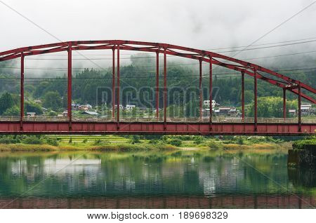 Bright Red Arch Bridge Over Picturesque River In Japanese Countryside