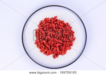 Dried Goji berries on a white ceramic plate with blue outer ring lines.  White background.