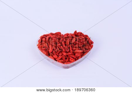 Dried Goji berries in heart shape plastic container with a white background.