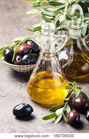 Olive oil in a glass bottle and olive branch on brown stone table