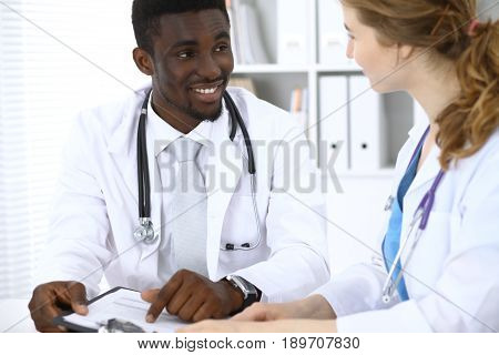 Happy smiling african american male doctor talking with colleague while sitting at the table.