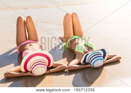 Sexy bikini body asian women enjoy the sea by laying down on sand of beach wearing millinery hat and both legs up in the air. Happy island lifestyle. White sand and crystal sea of tropical beach.