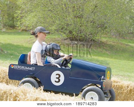 STOCKHOLM SWEDEN - MAY 21 2017: Smiling boy and mother driving a green soapbox car downhill on a field in the race Gardesloppet at Djurgarden Stockholm Sweden. May 21 2017
