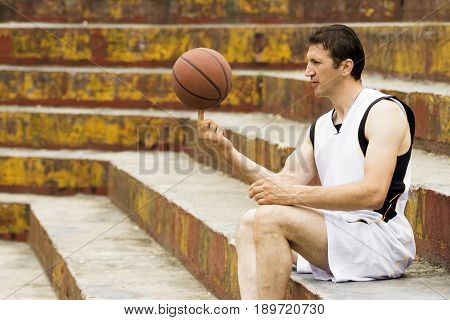 The playful basketball player is turning ball around on one finger and sitting on the steps.