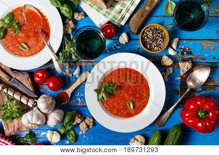 Tasty appetizing classic spanish soup gazpacho in white plates on rustic blue table with bread garlic and spices. Dinner Food Concept. Top View.