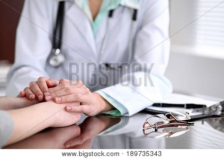 Friendly female doctor hands holding patient hand sitting at the desk for encouragement, empathy, cheering and support while medical examination. Bad news lessening, compassion, trust and ethics concept