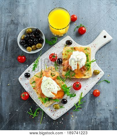 Poached egg on grilled toast with smoked salmon, rucola, olives, vegetables and orange juice. on white board. healthy breakfast.