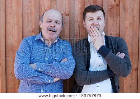 The Father-in-law And Son-in-law Standing By The Wooden Wall. They Are Tired And Bored.