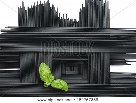 geometric arrangement of black squid ink spaghetti with a green basil garnish on a white background room for copy space