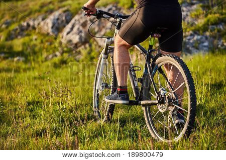 Close-up of detail of cyclist man feet riding mountain bike on rocky trail. Sportsman in the black shorts and with sportive shoes. Detail of the bike. Horizontal photo. Concept of the healthy and active lifestyle.