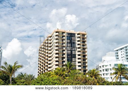 Miami beach or south beach. City skyline with white clouds on blue sky on sunny day. High rise apartment buildings or skyscrapers with green palm trees on foreground. Modern architecture.