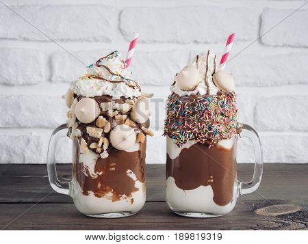 Close up view of two freakshake in mason jar on brown table. Freaked milkshake with chocolate, biscuit cookies and sugar sprinkling. Trendy food concept
