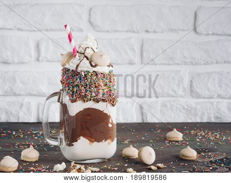 Close up view of freakshake in mason jar on brown table. Freaked milkshake with chocolate, biscuit cookies and sugar sprinkling. Copy space. Trendy food concept