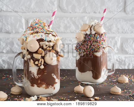 Close up view of two freakshake in mason jar on brown table. Freaked milkshake with chocolate, biscuit cookies and sugar sprinkling. Trendy food concept
