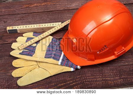Orange hard hat and gloves for work on wood background